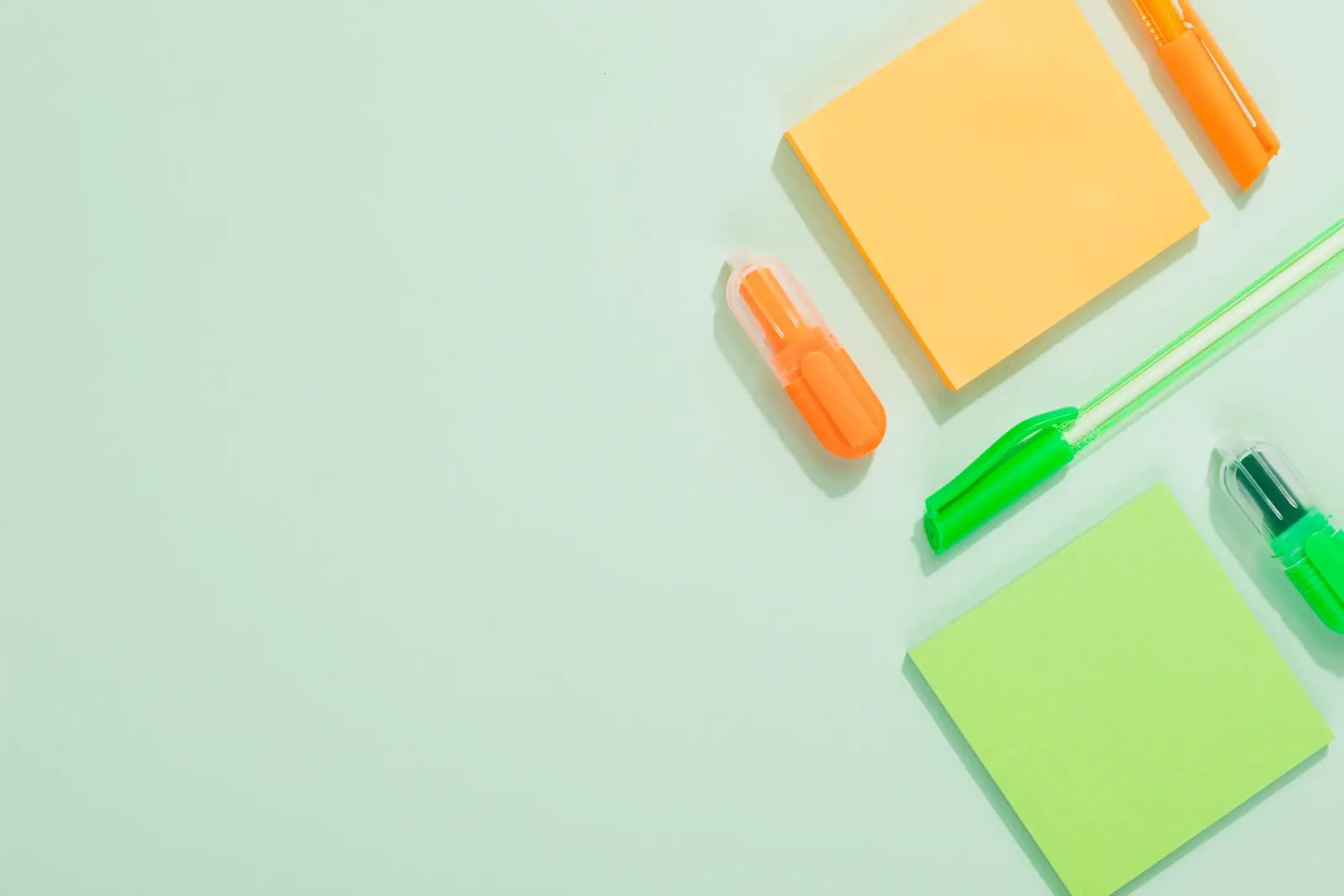 Orange and green notebooks, highlighters and pens arranged on a mint surface.