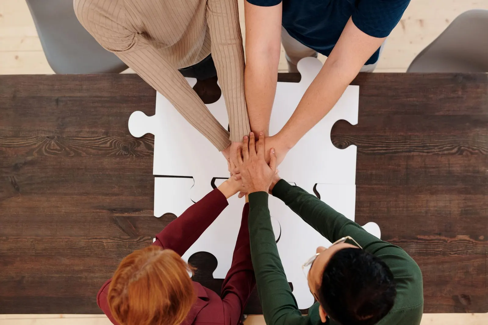 An overhead view of a group joining hands above interlocking white puzzle pieces.