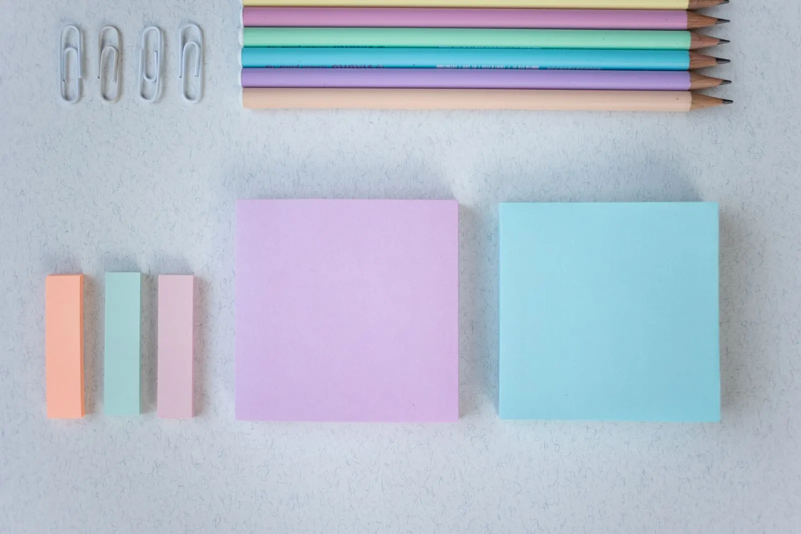 Pastel note pads, coloured pencils and paper clips arranged in tidy rows.