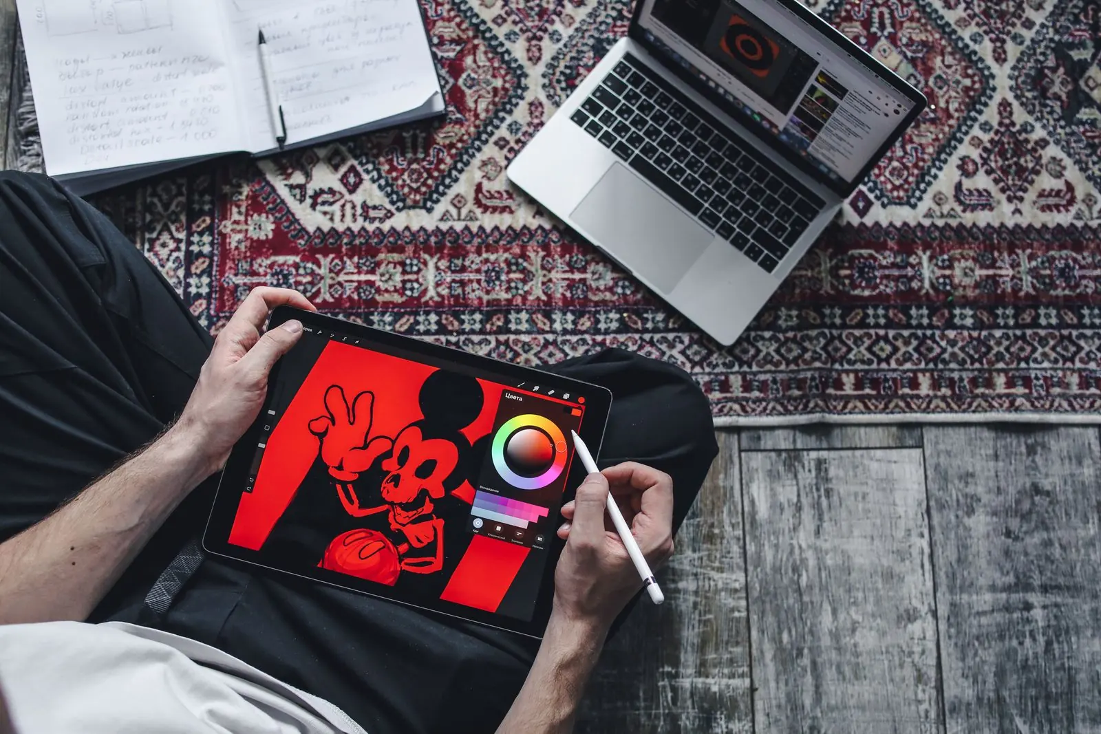 A person uses a stylus to draw a red cartoon on a tablet beside a laptop.
