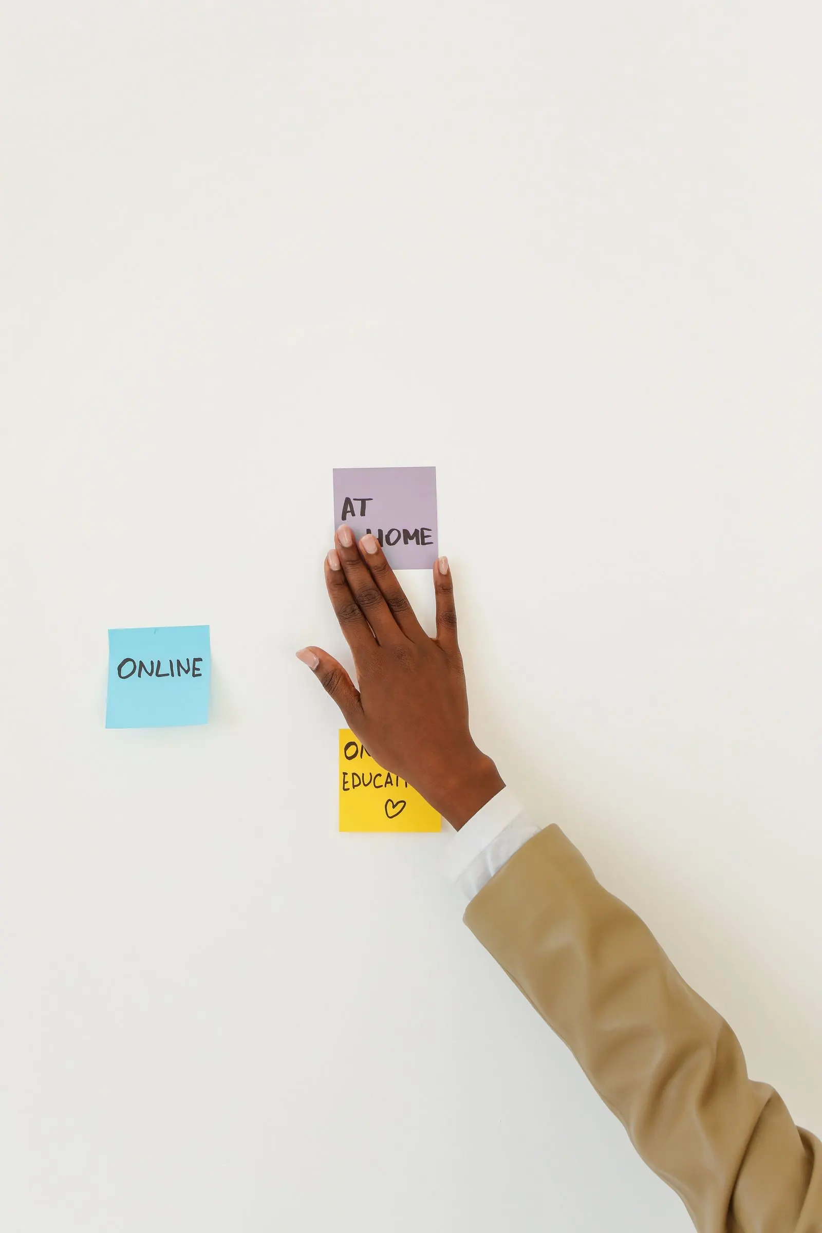 A hand adds a pink note to a small cluster of colourful planning notes on a wall.