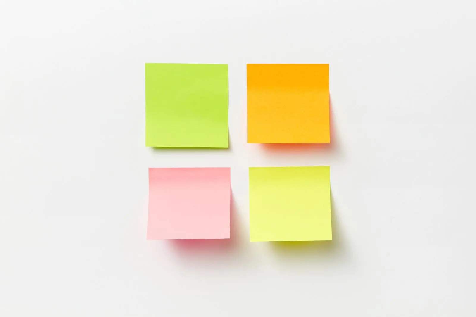 Four yellow, green and pink sticky notes form a square on a white surface.