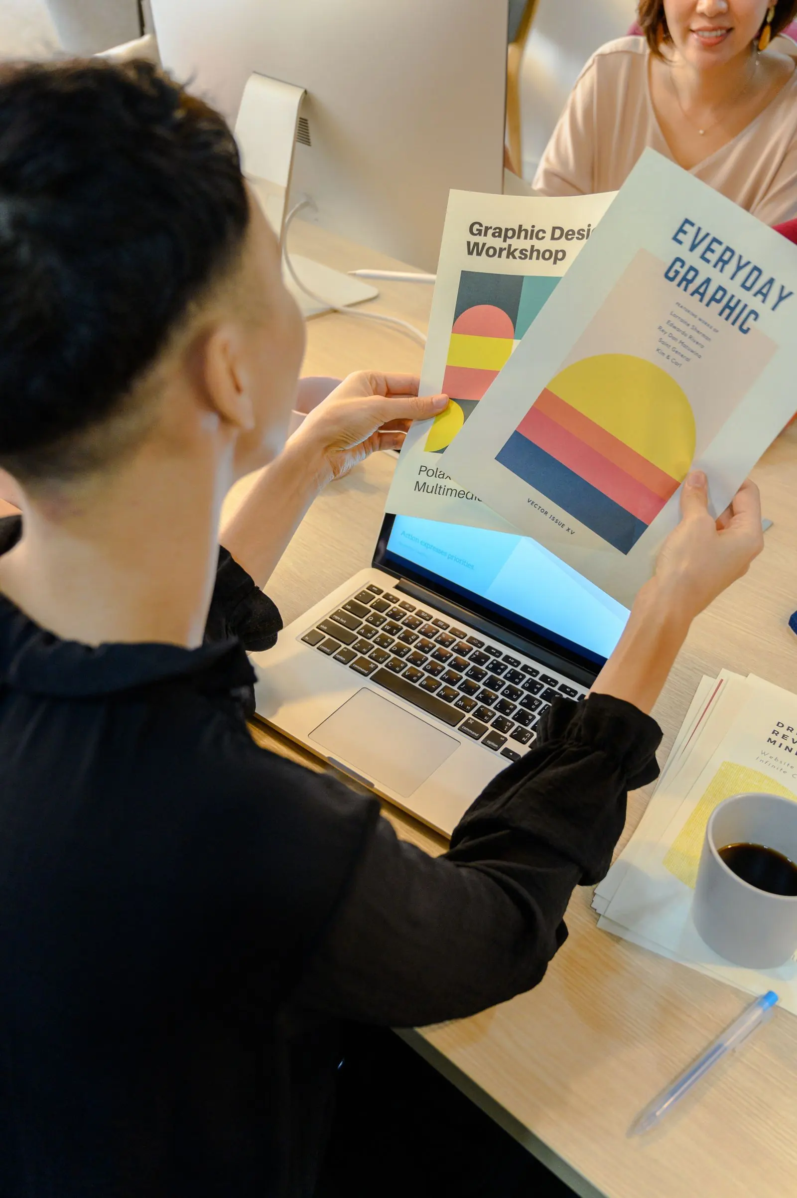 A person reviews a colourful printed diagram beside an open laptop.