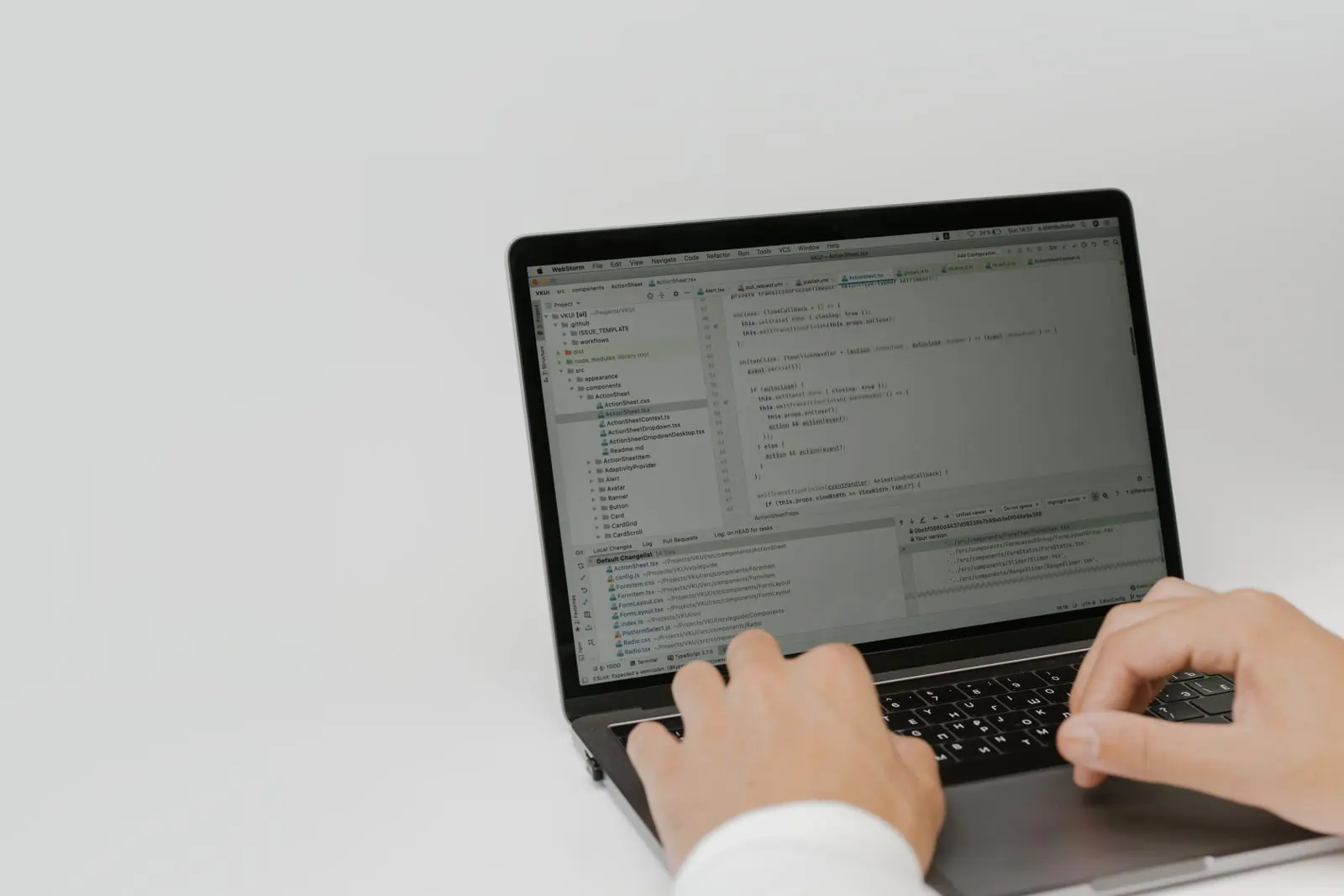 Hands type source code on a laptop against a plain light background.