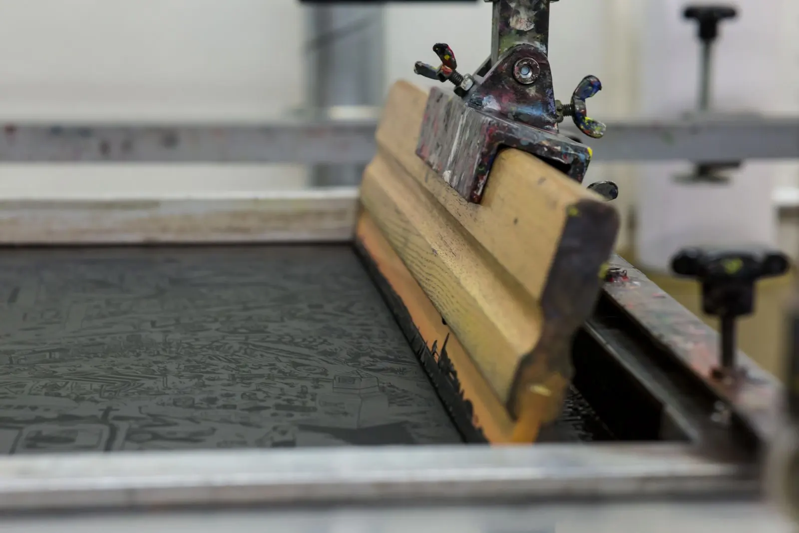 A close view of an orange squeegee resting across an ink-stained screen-printing frame.