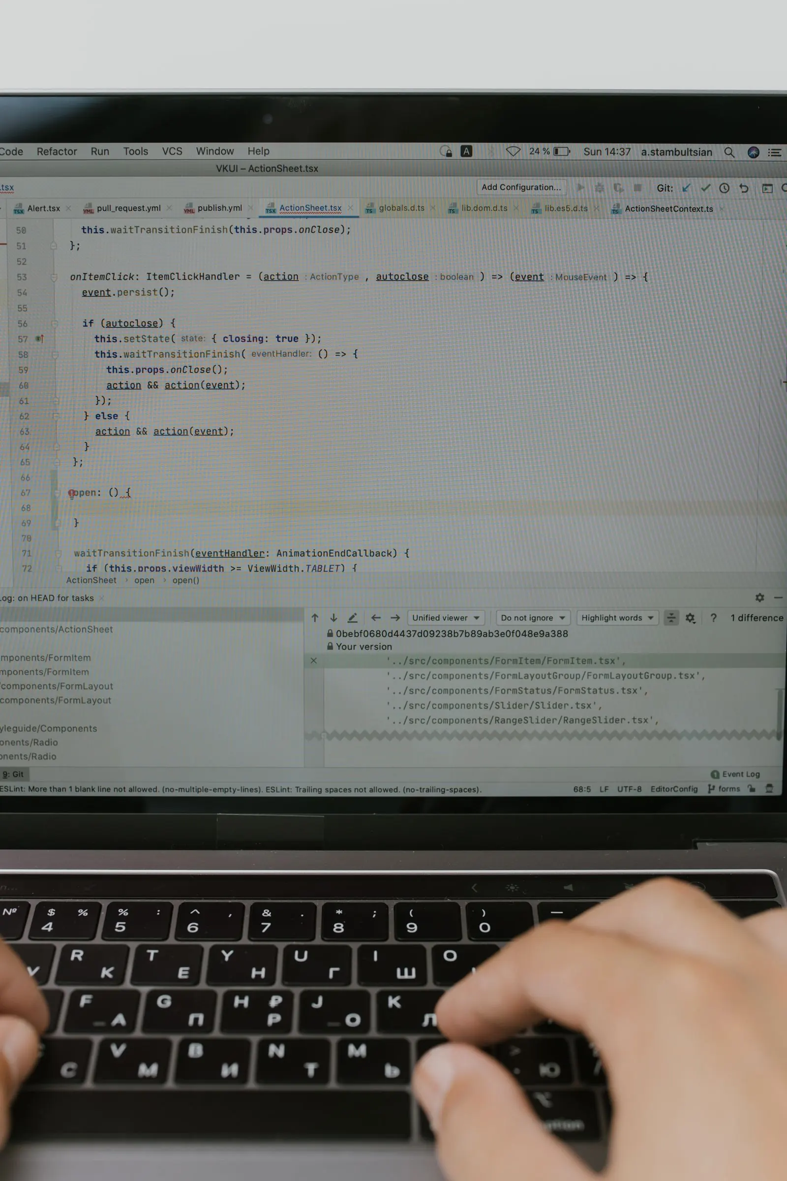 A hand works at a laptop with source code open in a text editor.