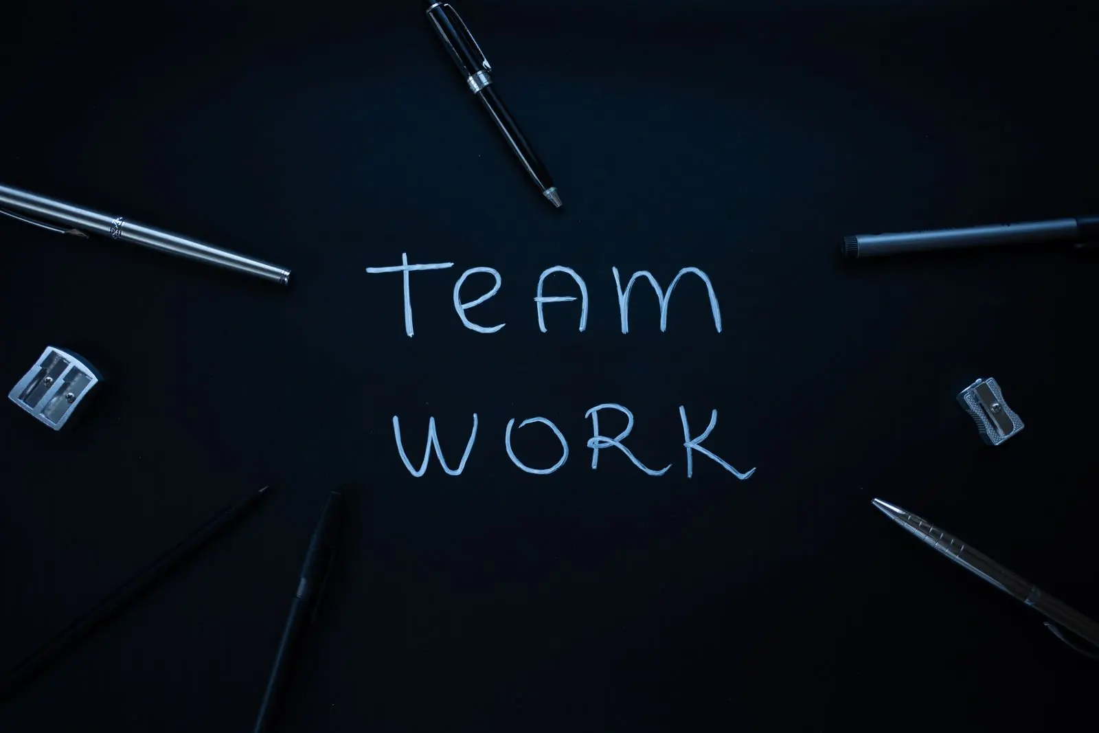 The words team work are written in white chalk on a dark surface beside pencils.