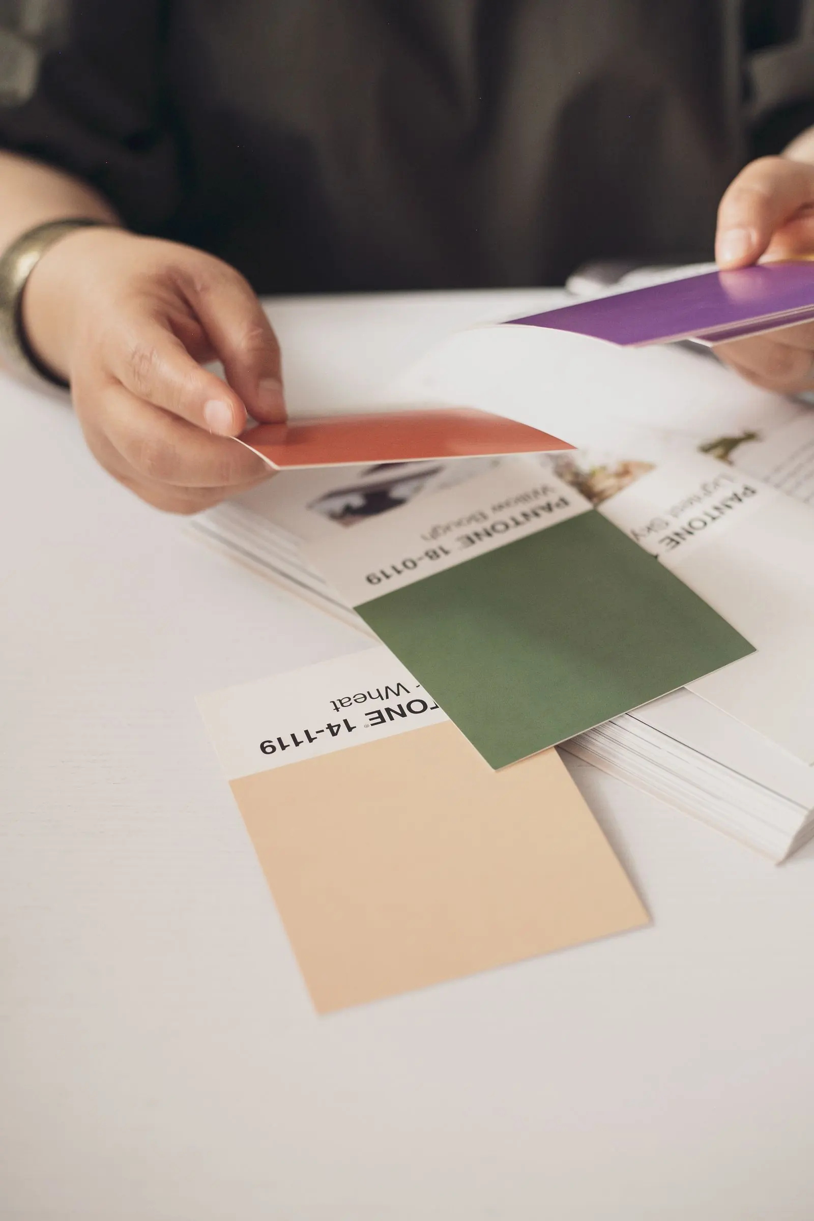 Hands compare coloured card samples with a printed design sheet.